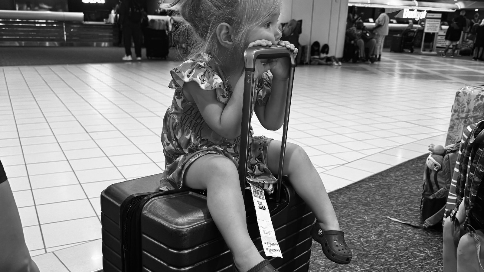 Young girl sitting on a suitcase at the airport ready for the family's move from Vermont to Northeast Florida